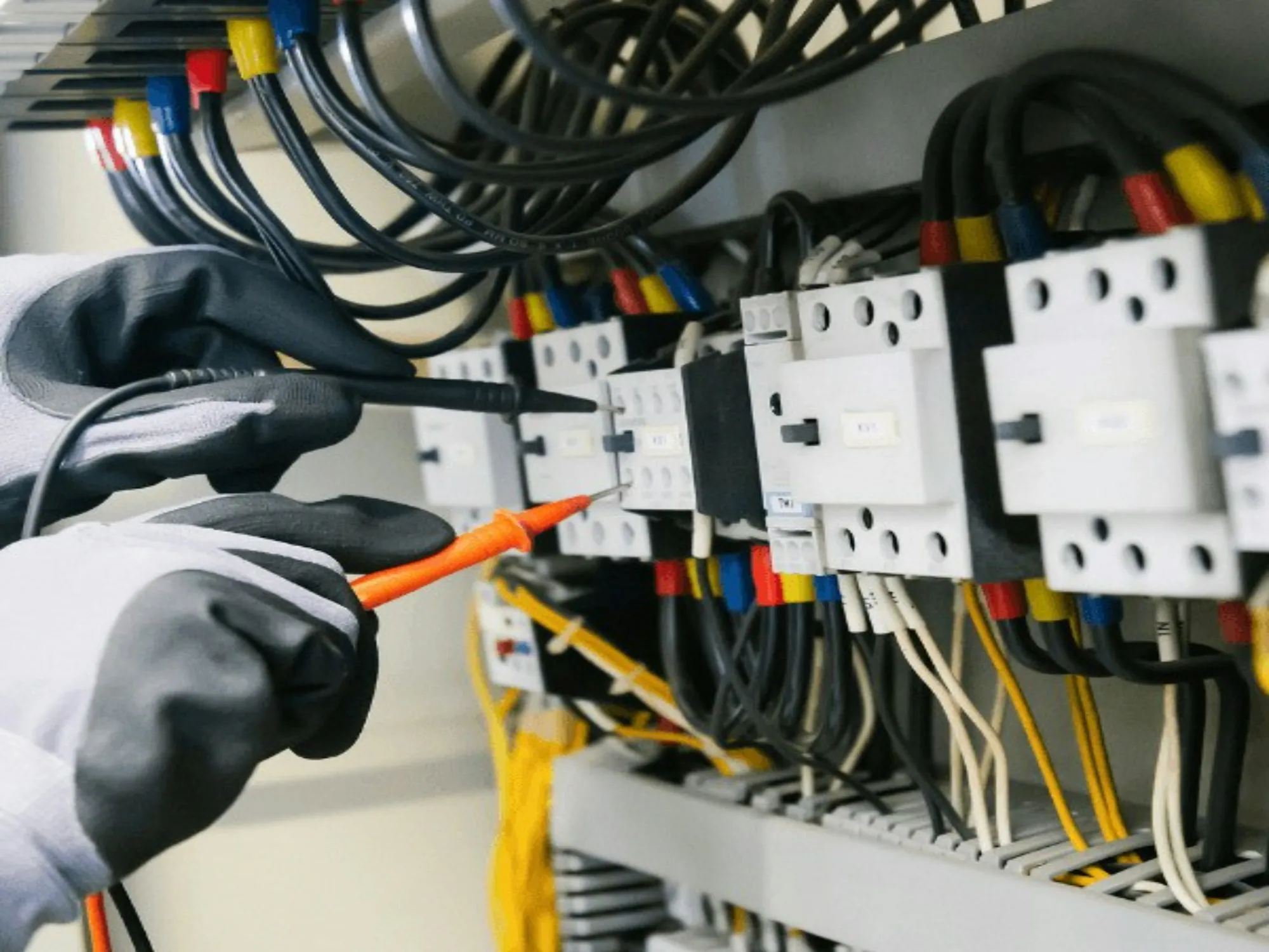 Gloved hand testing breakers in an electrical panel
